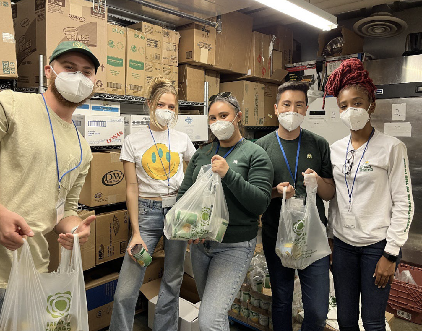 Five team members stand in a Safe Haven Foundation storage room, holding bags of donated goods.